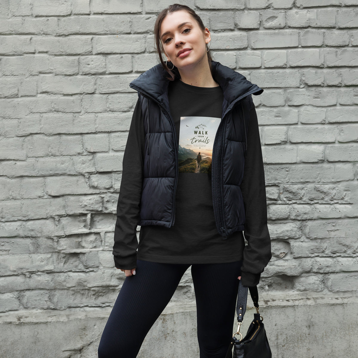 Unisex Long Sleeve Tee, Woman wearing a black puffer vest over a graphic t-shirt against a brick wall.